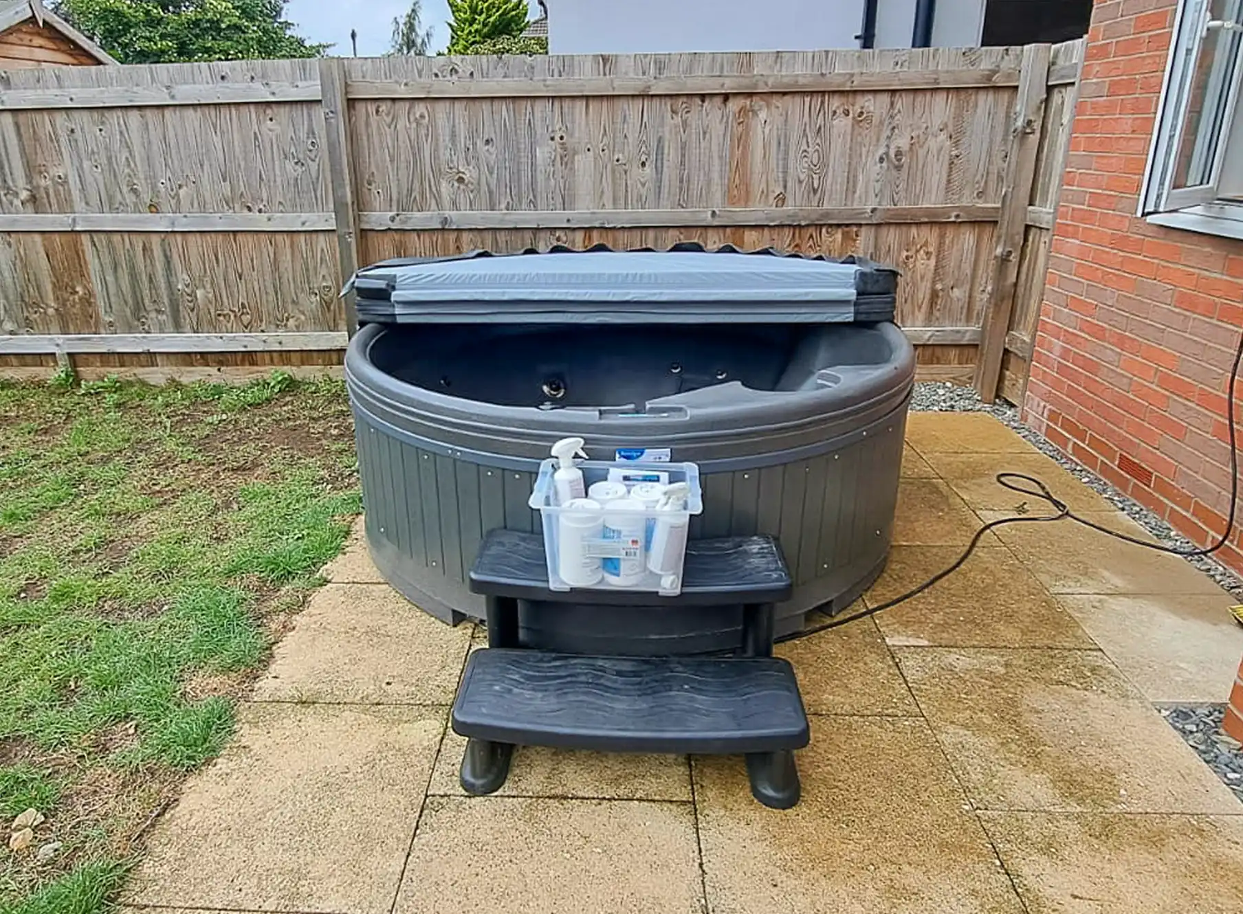 Round hire hot tub sat on patio with steps in front. The include chemical kit is sat on the step ready for customer to use.