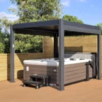American Whirlpool 881 sat on wooden decking with a grey Maze Living pergola over it for shelter. Hot tub with mocha colour cabinet and white shell. Black steps and a cover lifter.