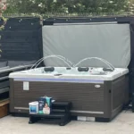 American Whirlpool 881 with a white silver marble shell and charcoal grey cabinet say on patio with black steps and a heat pump fitted. A gas assisted cover lifter fitted for easy opening. 4 Waterfalls arcing over the water and purple LED lights shining