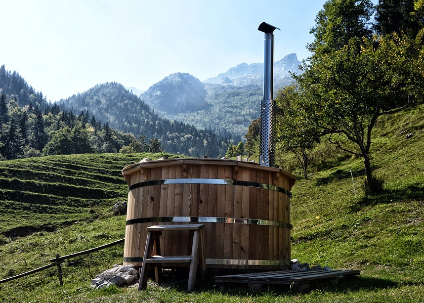 a wooden hot tub with sood steps say in field with mountain backdrop