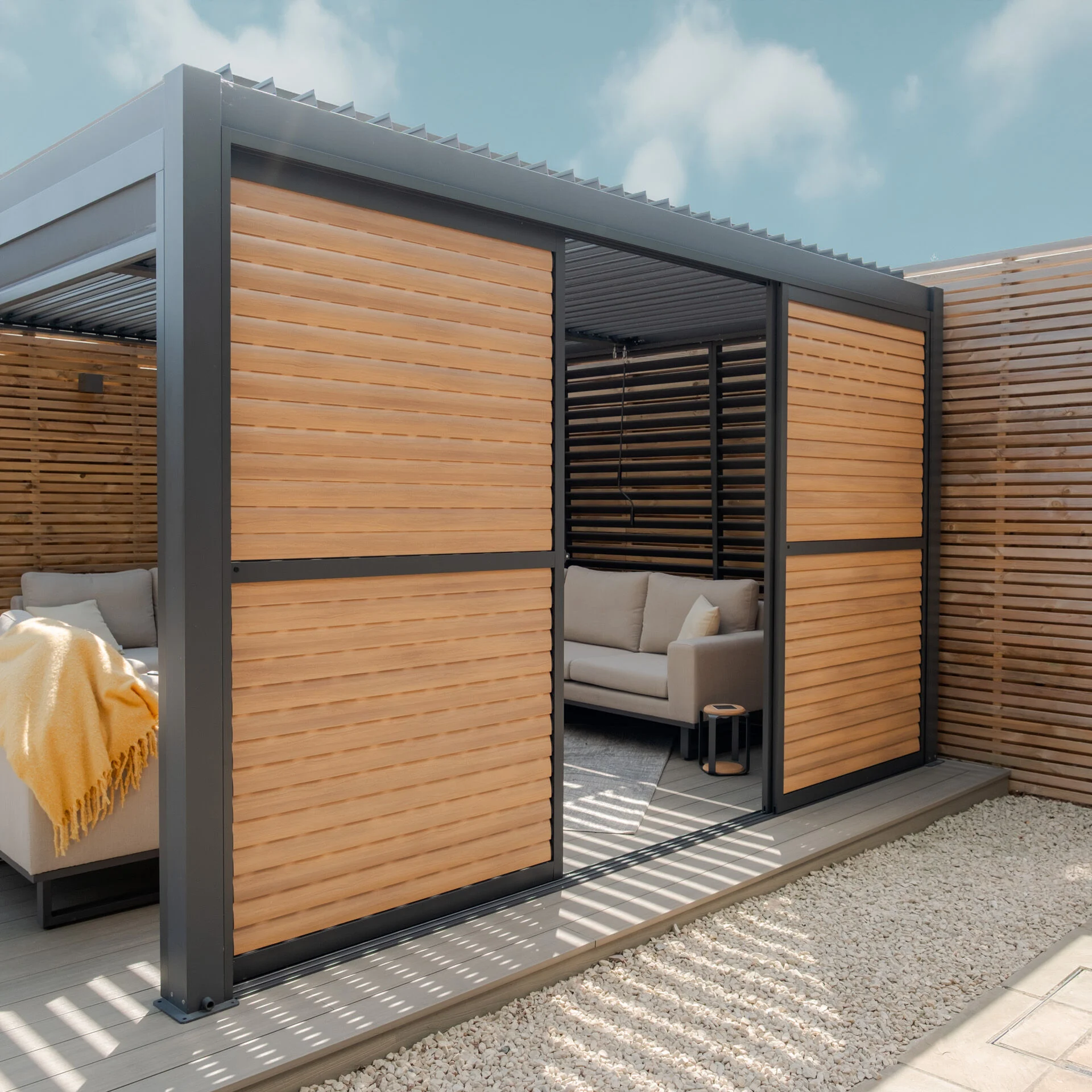Maze Living Como pergola in dark grey with wood effect adjustable louvres with slats angled closed and one door slid open to give gap in the middle to walk through.