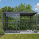 Maze Como grey pergola with transparent sliding doors fitted to two sides. Pergola sat on a light grey patio surrounded by l;awn with a green hedge behind.